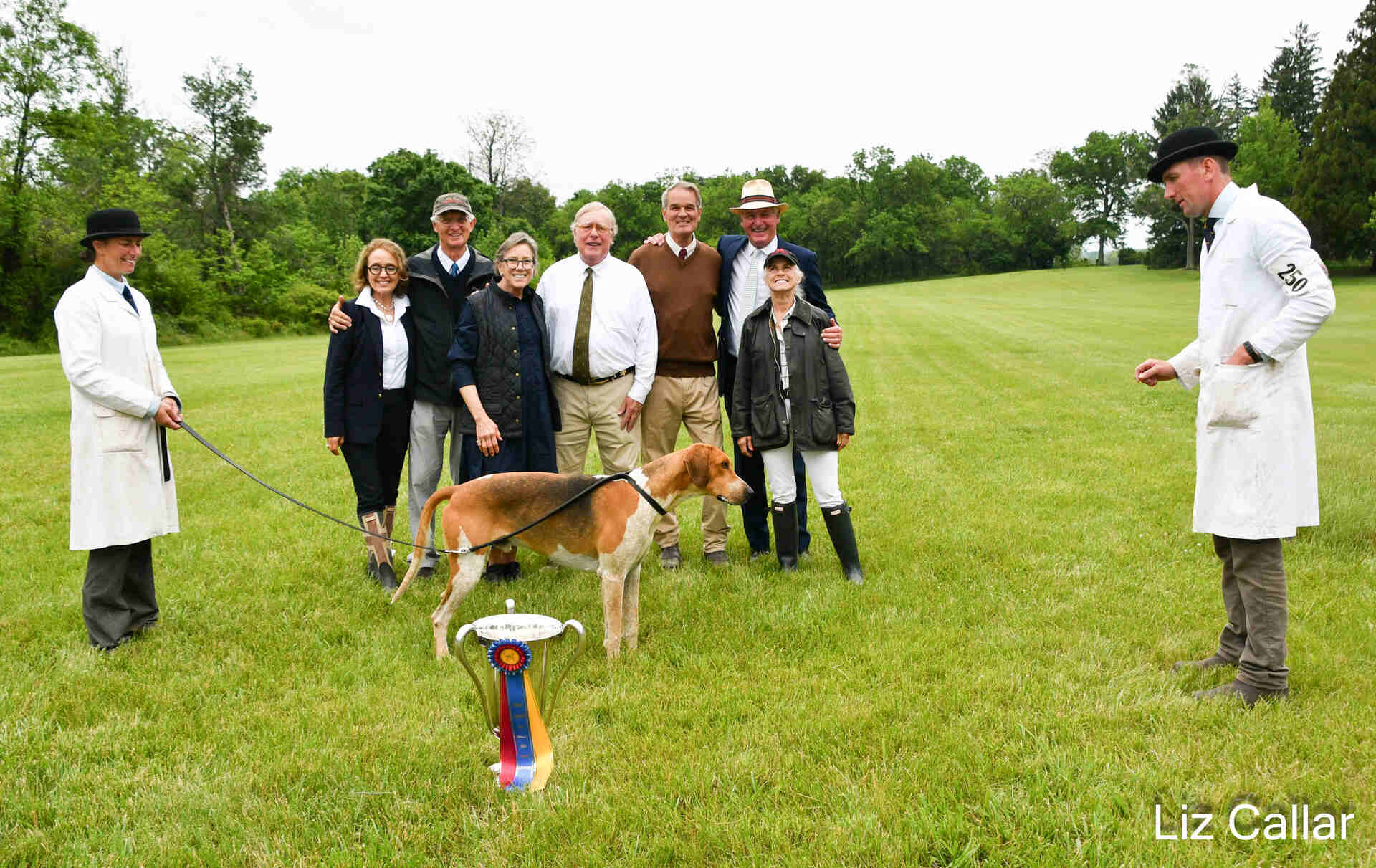 Hound with handlers, trophy, ribbon, and several people
